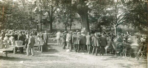 Old black and white photo of farmers at outdoor meeting.
