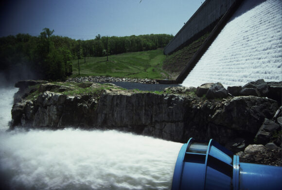 Trees, rocks, and waterway with water gushing out of a large pipe and flowing down a spillway