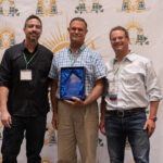Three people posing for a picture, the middle one holds an award