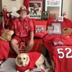 A man posing with his dogs and displaying items from his alma mater