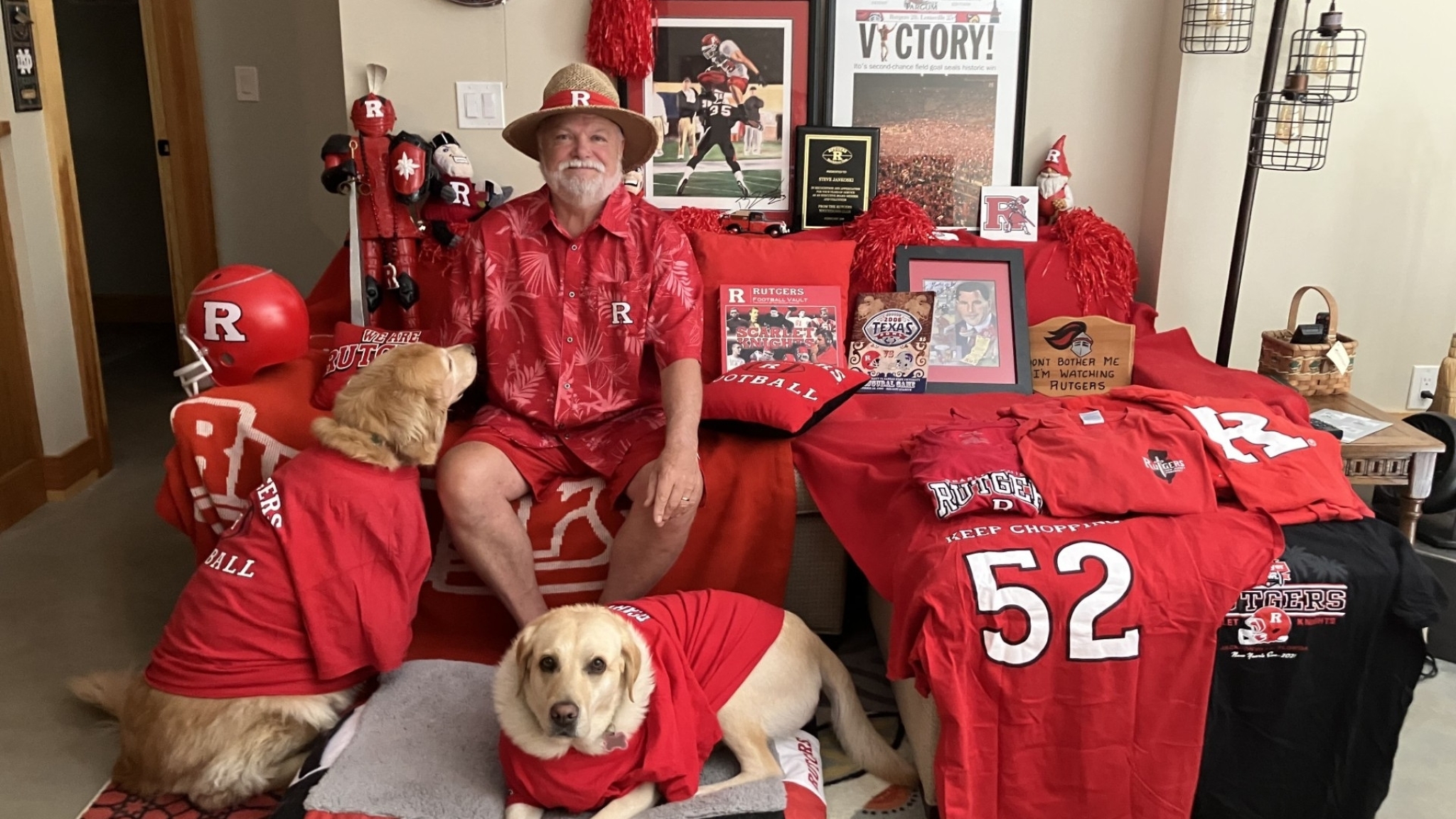 A man posing with his dogs and displaying items from his alma mater