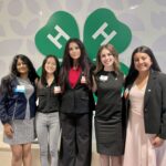 Five 4-H members stand in front of a 4-H logo