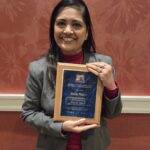 A woman smiles and holds the 2025 Distinguished Service Award at the National Extension Association of Family and Consumer Sciences (NEAFCS) Annual Session.