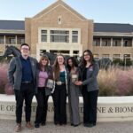 A group of five persons standing in front of a building