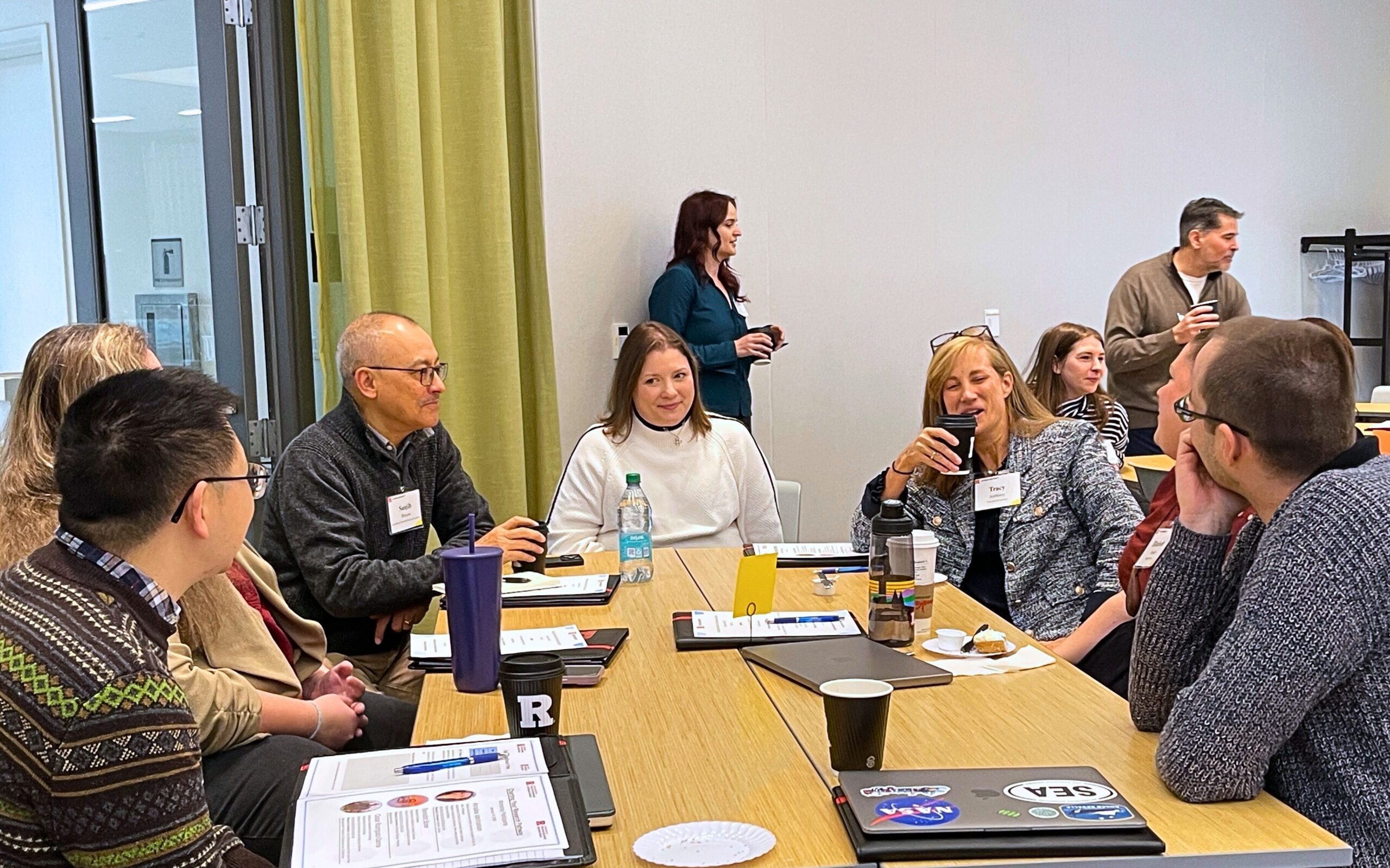 Seven people sit around a table, chatting over coffee.