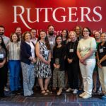 A large group posing in front of a large Rutgers sign affixed to a wall.