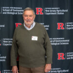 A person posing in front of a Rutgers University New Jersey Agricultural Experiment Station banner