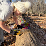 A person sawing a log that has colorful clear acrylic pieces connected to it