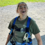 A person wearing rock climbing gear smiles at the camera