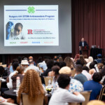 A man stands at a podium presenting about the Rutgers 4-H STEM Ambassadors Program to a room of people