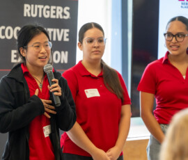 Three students standing together while one speaks into a microphone