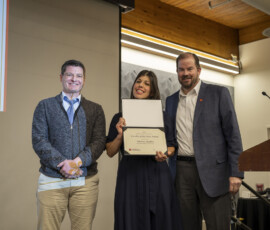 Three people posing for a photo while one holds an award